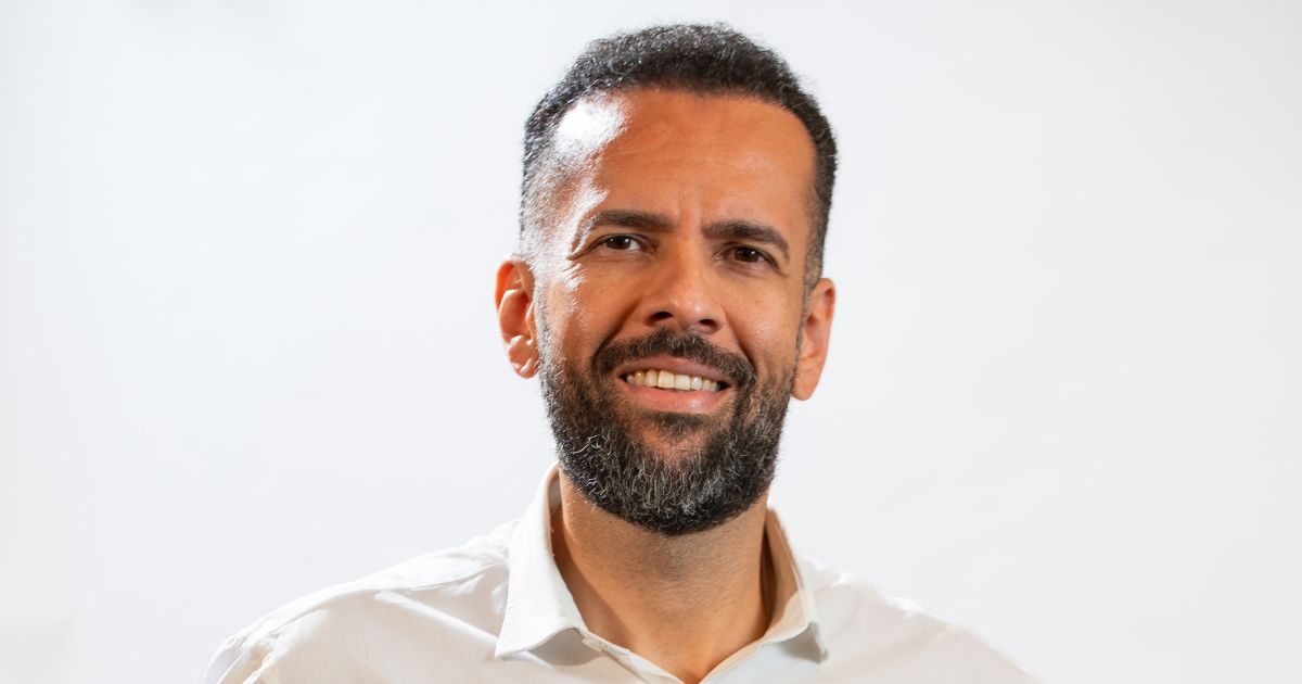 A imagem mostra a parte superior de uma pessoa vestindo uma camisa social branca, posicionada diante de um fundo uniforme e claro. O enquadramento captura cabeça, ombros e parte do torso, com iluminação suave destacando a roupa e os contornos do sujeito. (Gerdau)