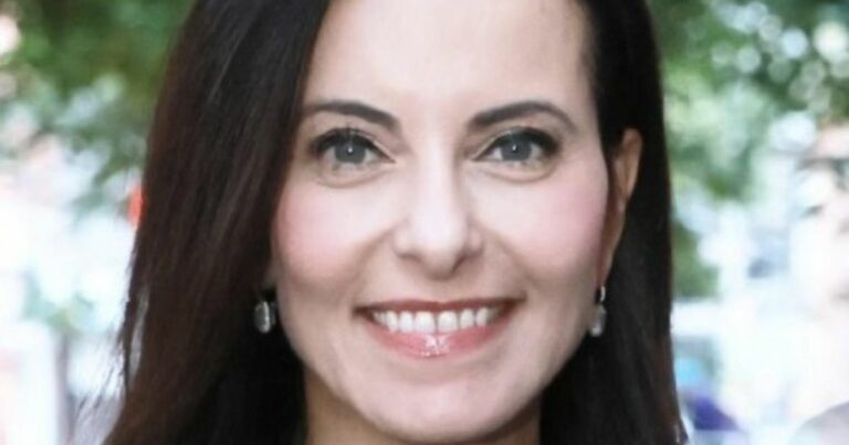 A imagem mostra uma pessoa com cabelo escuro e liso, usando um brinco pequeno e arredondado, em um ambiente externo com fundo desfocado, sugerindo árvores ou vegetação. A iluminação é natural, indicando que a foto foi tirada durante o dia. O enquadramento é um close-up, destacando a parte superior do corpo e os detalhes do cabelo e acessórios. O fundo verde e claro cria contraste com os tons mais escuros do cabelo e da roupa. (Meta e Dina)