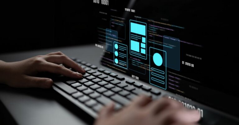 A imagem mostra um teclado sendo utilizado por uma pessoa, com uma tela digital projetando elementos gráficos e códigos. Detalhes principais: Primeiro plano: Mãos digitando em um teclado, sugerindo atividade de programação ou desenvolvimento. Tela projetada: Exibe códigos em linguagem de programação e elementos de interface (UI) como caixas, ícones e layouts, indicando design e desenvolvimento de aplicações ou sites. Cores e estilo: Fundo escuro com destaques em azul neon para os elementos gráficos, transmitindo uma estética tecnológica e futurista. Contexto: Representa claramente um cenário de desenvolvimento digital, programação e inovação tecnológica. (BRQ)