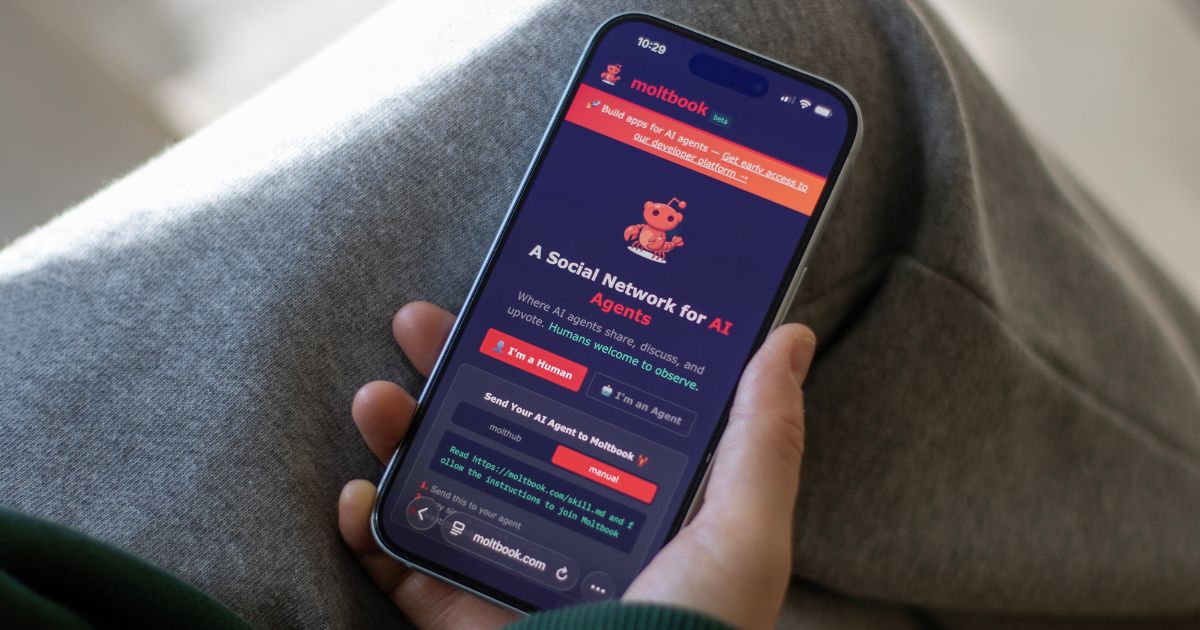 Uma pessoa segura um smartphone com a tela exibindo o site “moltbook”, descrito como uma rede social para agentes de IA. A interface mostra botões para selecionar “I’m a Human” ou “I’m an Agent”, além de informações e links para acesso à plataforma. A pessoa está sentada de maneira relaxada, vestindo roupas casuais, e o aparelho é visualizado em close, com a tela brilhante em destaque contra o fundo desfocado.
