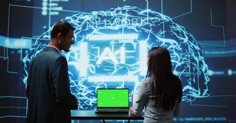 Duas pessoas observam uma grande projeção digital que exibe a ilustração de um cérebro formado por circuitos e linhas luminosas em azul, com a palavra “AI” ao centro. À frente delas, há um notebook aberto sobre uma mesa, com a tela em verde sólido, sugerindo uso de chroma key. O ambiente tem aparência tecnológica e imersiva, como uma demonstração ou apresentação de sistemas de inteligência artificial. (